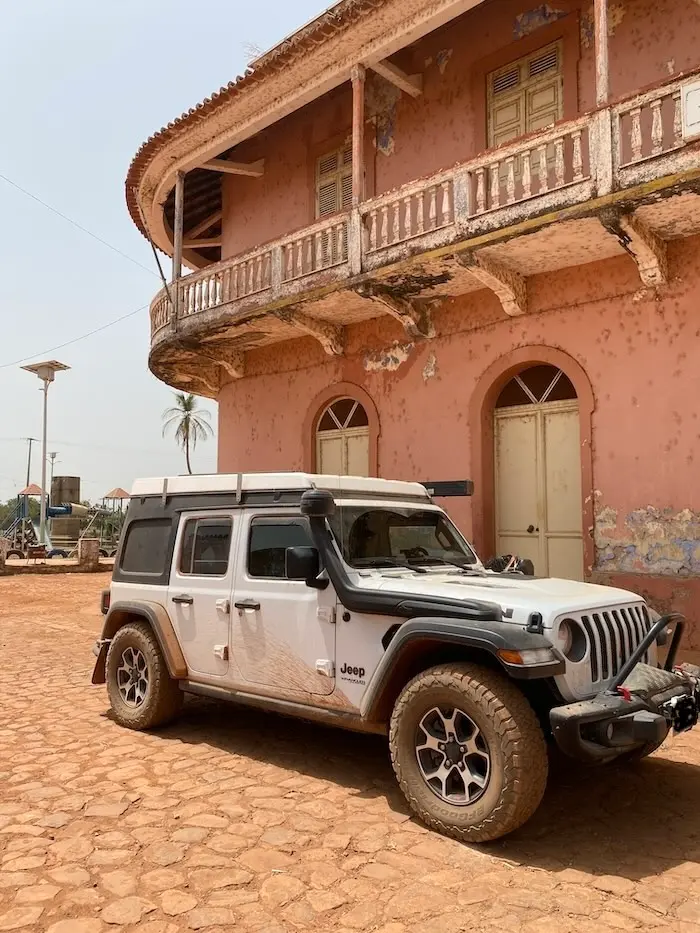 Jeep Wrangler Rubicon parked in front of a colonial-era French building in Bafata, Guinea-Bissau during an Africa overland expedition