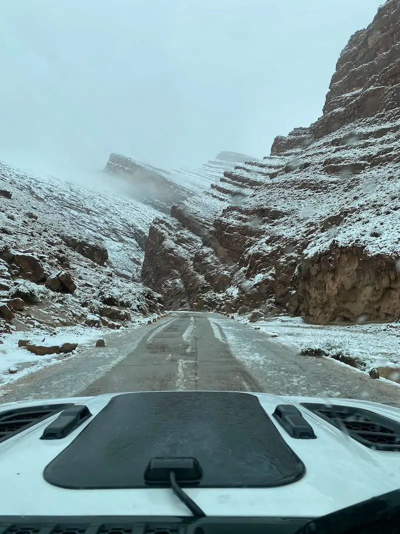 View from inside a Jeep Wrangler Rubicon driving through Todra Gorge in Morocco, showing the road ahead and dramatic Atlas Mountains landscape through the windshield
