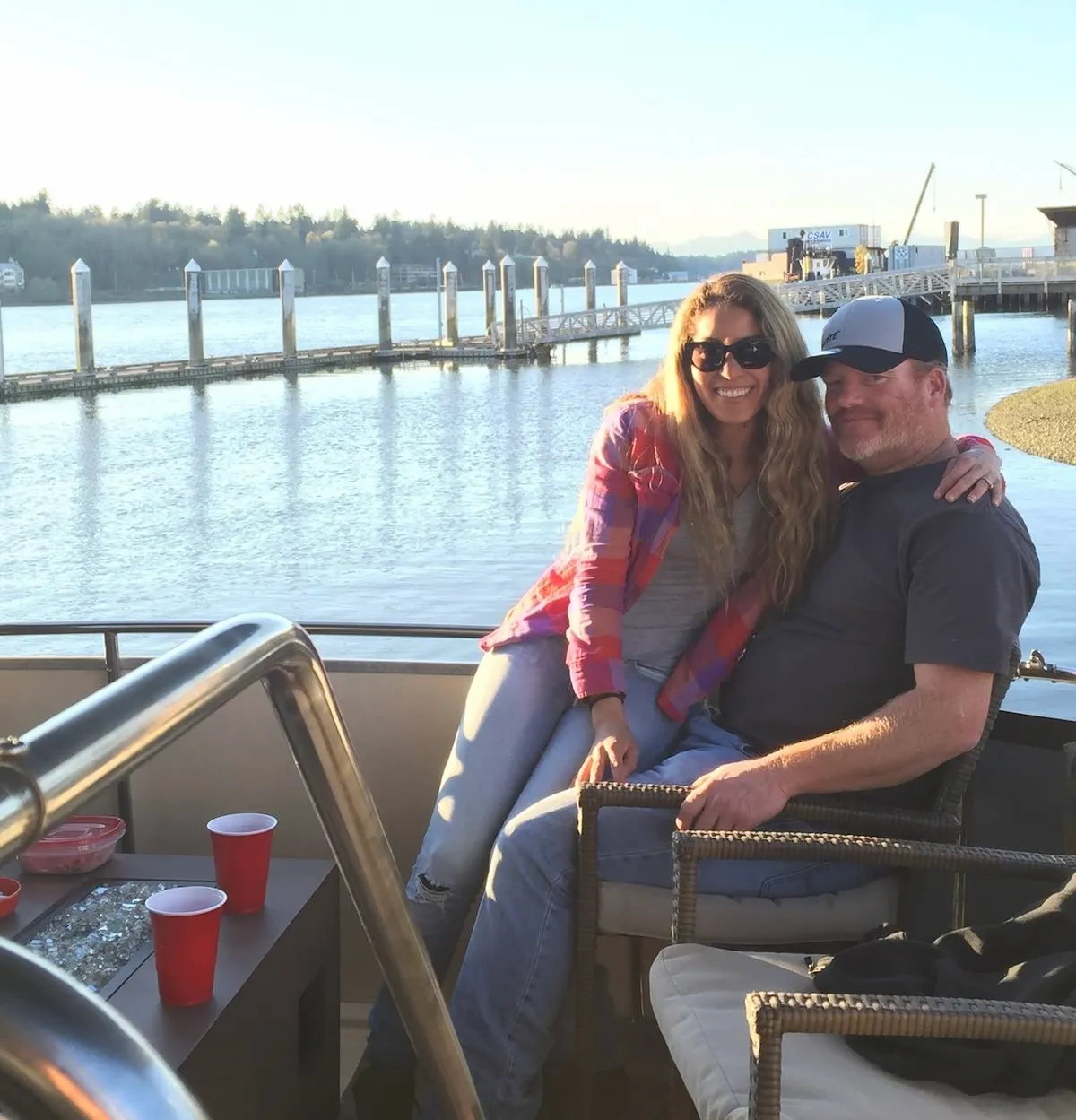 Brett and Karla sitting on the deck of a boat with a marina and water in the background