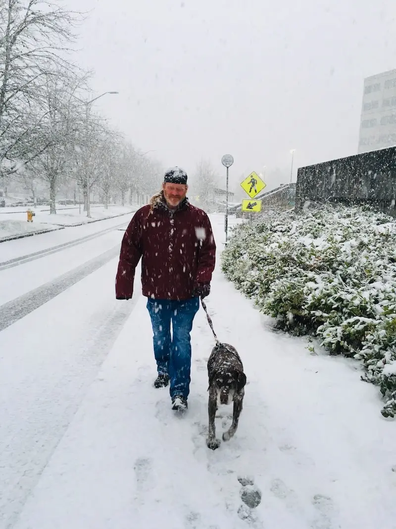 Brett walking his dog on a snowy street during a snowfall