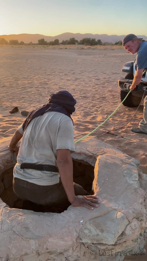 Camel herder beginning to descend into a desert well during a baby camel rescue in Morocco