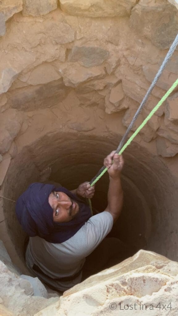Camel herder inside a desert well holding the winch and safety lines while being lowered to rescue a baby camel in Morocco