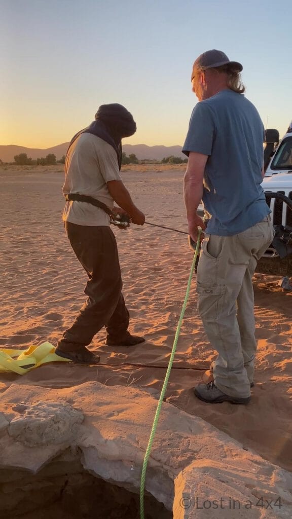 amel herder preparing to descend into a desert well with a winch line while Brett secures the safety line during a baby camel rescue in Morocco