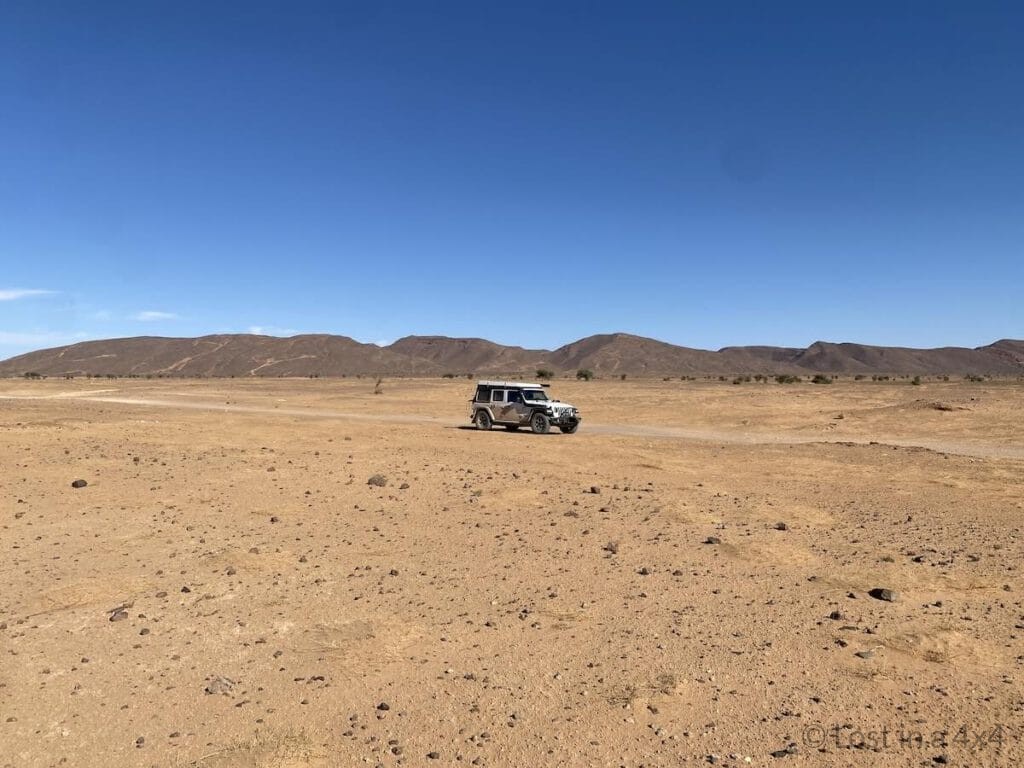 Jeep driving a 4x4 desert track from Rissani to Ramlia with mountains in the background in Morocco