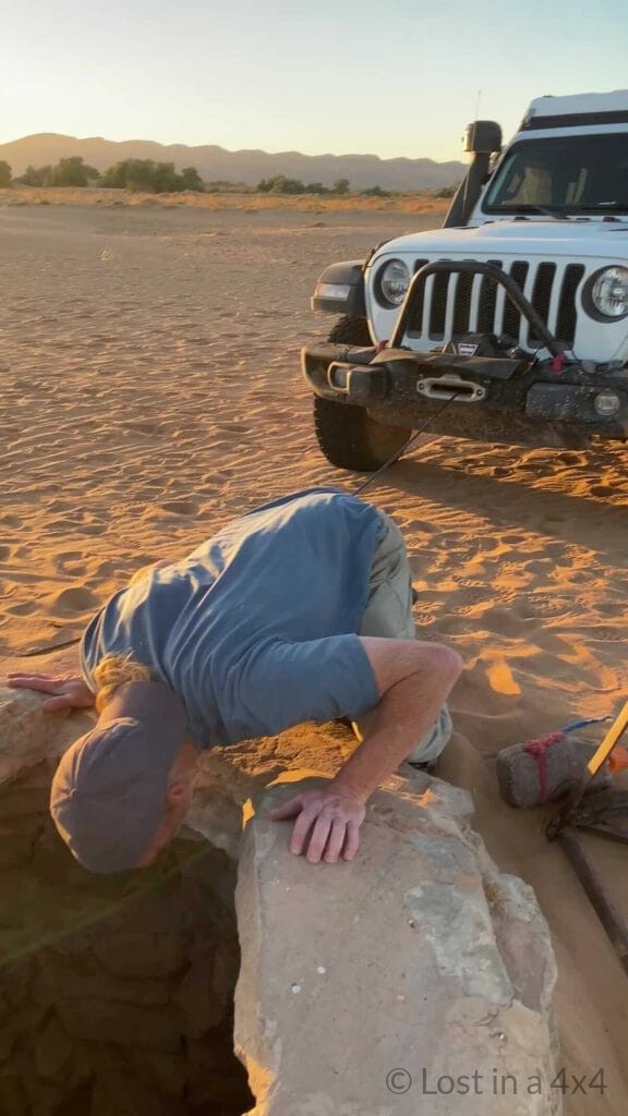 Brett looking down a desert well to assess a baby camel rescue with the Jeep nearby in Morocco