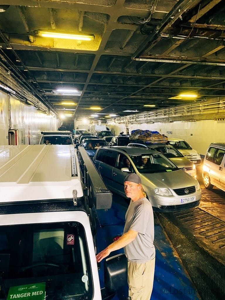 Brett standing beside a Jeep on the lower deck of a ferry in Tangier Med, Morocco, waiting to disembark with other vehicles