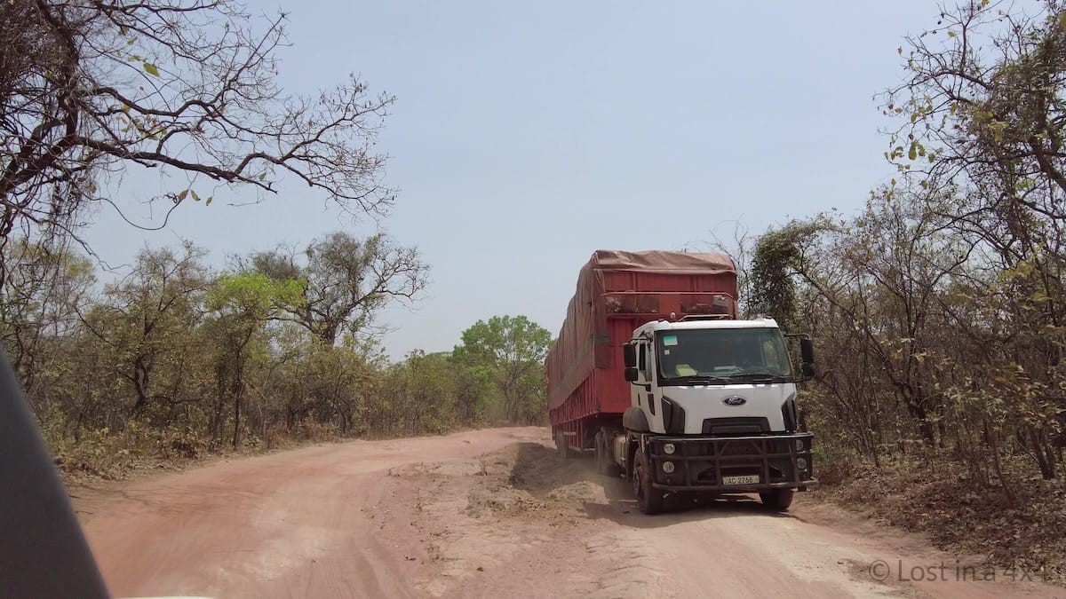 View through Jeep windshield of a rough dirt road in Guinea with an oncoming truck during an overland journey.