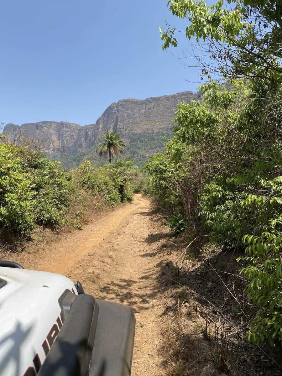 Jeep driving on yellow dirt road in Guinea with sheer cliffs ahead during overland Africa expedition