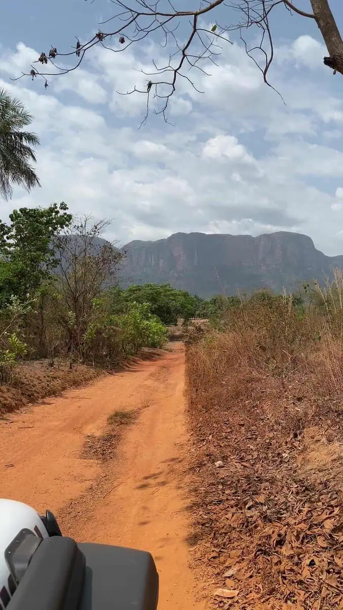 Jeep driving on red dirt road in Guinea with sheer cliff mountains rising ahead during overland Africa trip
