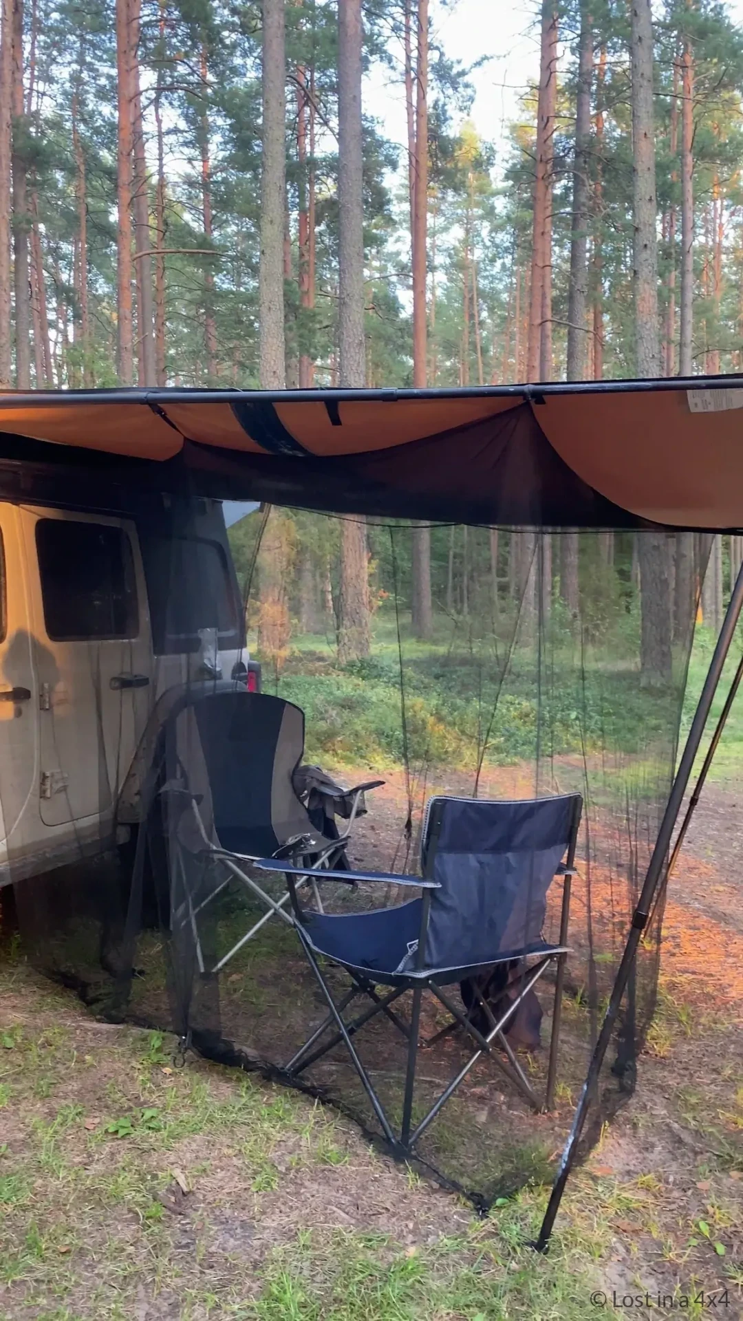 Mosquito net attached to an ARB Touring Awning beside a Jeep, with two camping chairs inside the protected outdoor living area during an overlanding trip.