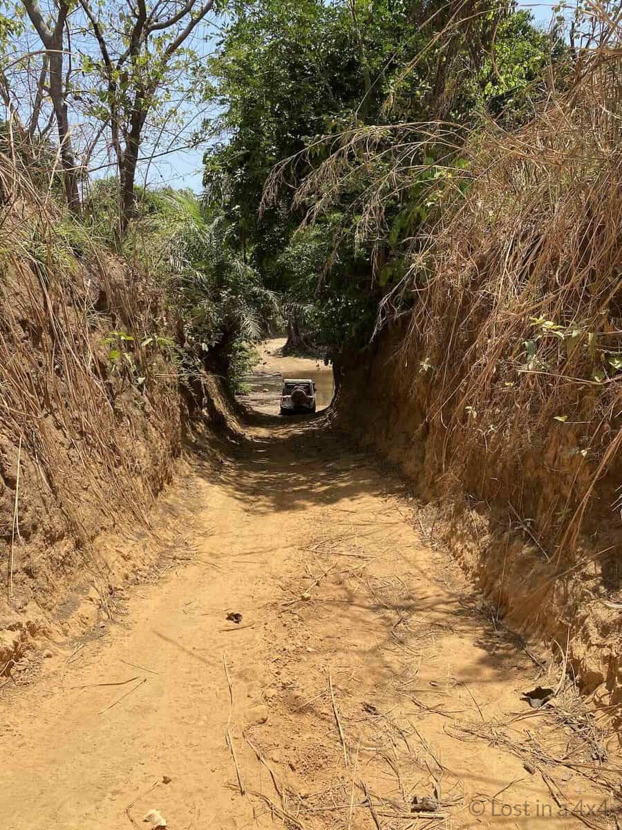 Jeep Wrangler Rubicon stopped at small creek at end of narrow dirt tunnel road in Guinea mountains during overland Africa trip