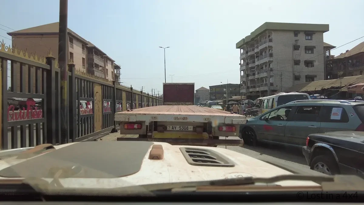 View from inside a Jeep Wrangler windshield showing a large truck ahead being used as cover in heavy traffic in Conakry, Guinea