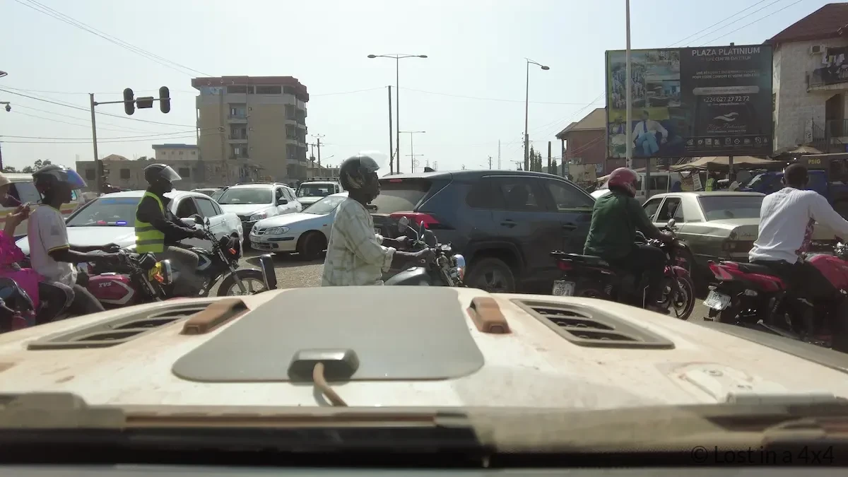 View from inside a Jeep Wrangler windshield showing heavy traffic in Conakry, Guinea just before a vehicle collision ahead