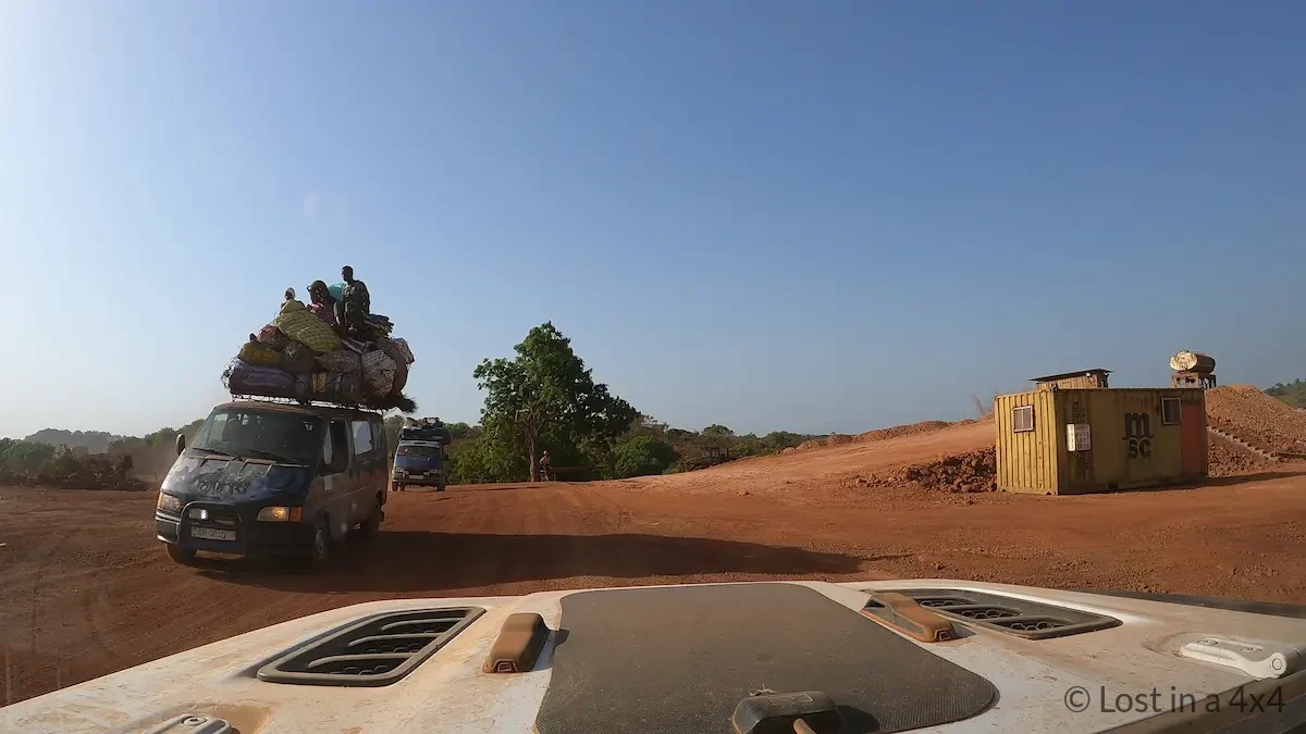 Inside view from our Jeep Wrangler Rubicon on the road to Conakry, Guinea, showing two oncoming minibuses heavily loaded with cargo and passengers seated on top, highlighting everyday transport conditions along this West African route