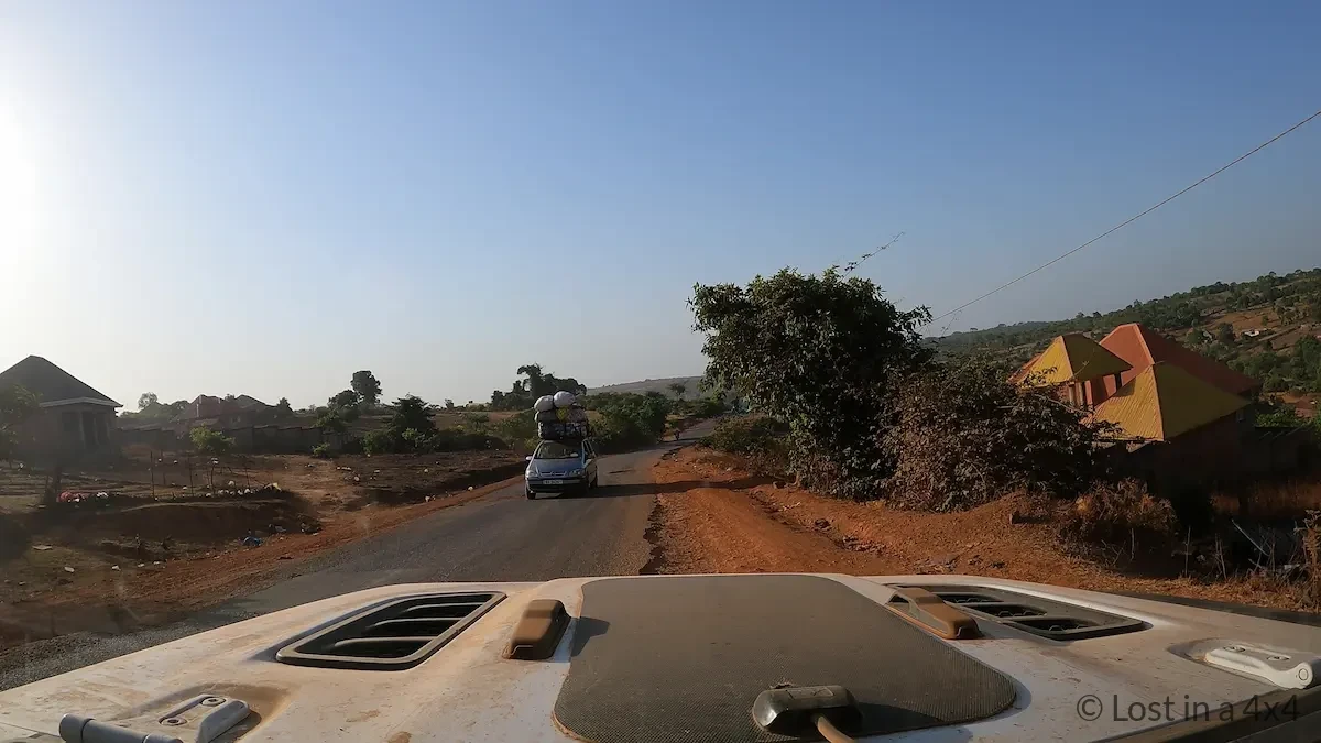 View from inside a Jeep Wrangler windshield showing a rough road to Conakry, Guinea with an overloaded vehicle approaching on the opposite side