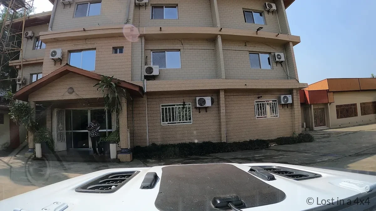 View from inside a Jeep Wrangler windshield showing the front of Zambezi Inn Hotel in the parking lot near Conakry airport, Guinea