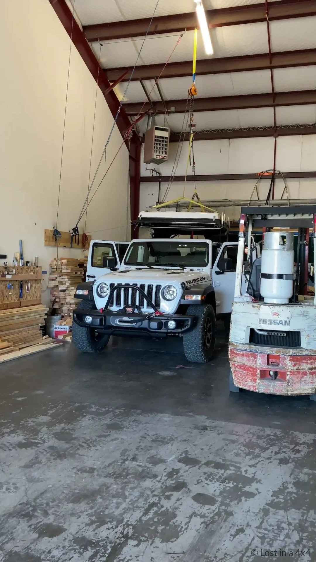 Ursa Minor pop-top roof camper being lowered onto a Jeep Wrangler Rubicon during installation in an Oregon workshop.