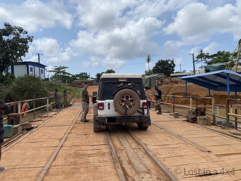 Jeep Wrangler and Brett standing on ferry crossing the Cavalla River between Liberia and Côte d’Ivoire during overland border crossing.