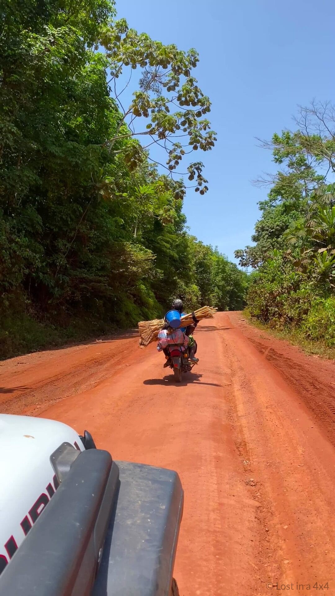 Jeep Wrangler driving on a red dirt road in Liberia behind a motorcyclist during overland Africa travel.