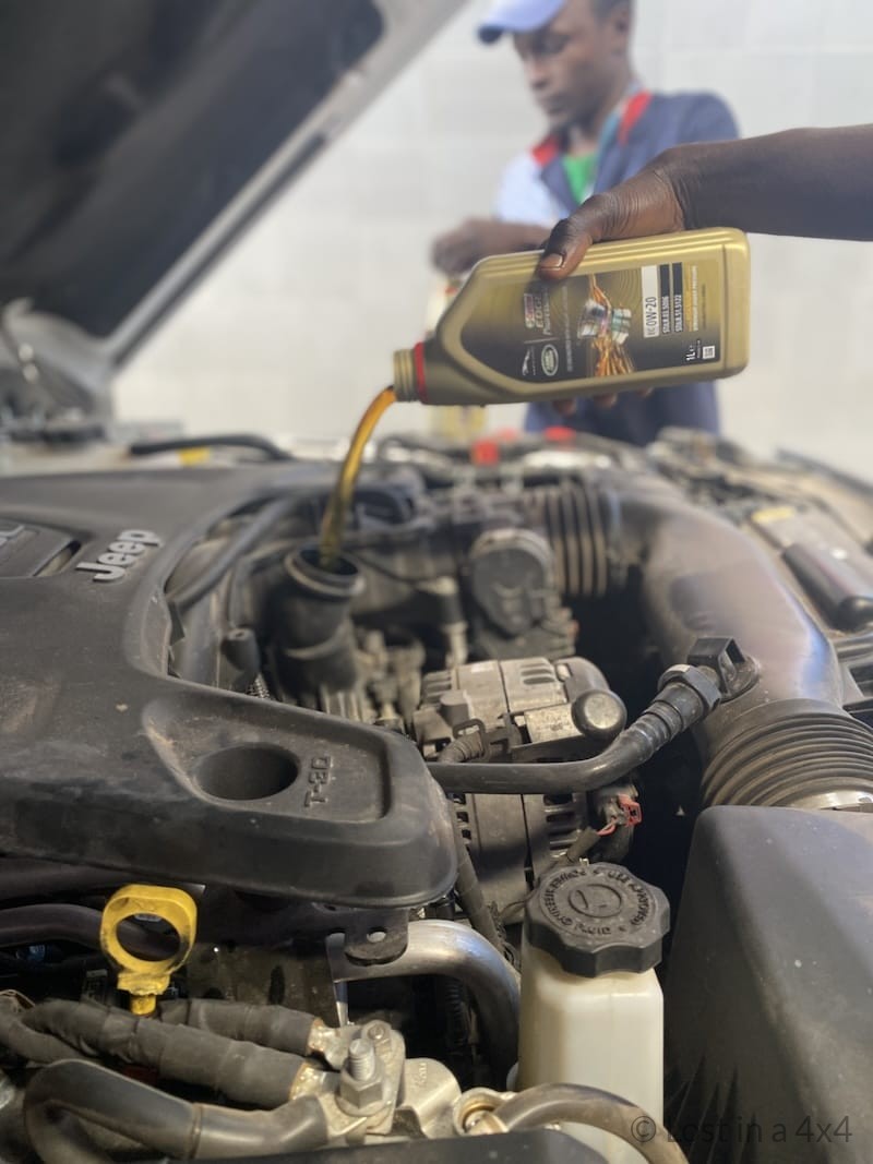 Mechanic adding new engine oil to an overland Jeep in Dakar Senegal.