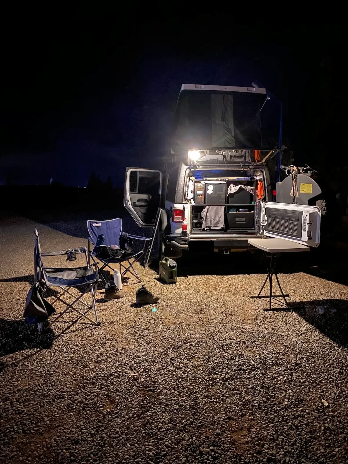 Onite USB rechargeable camping lights hanging from the rear window of a Jeep Wrangler illuminate an overland campsite at night.