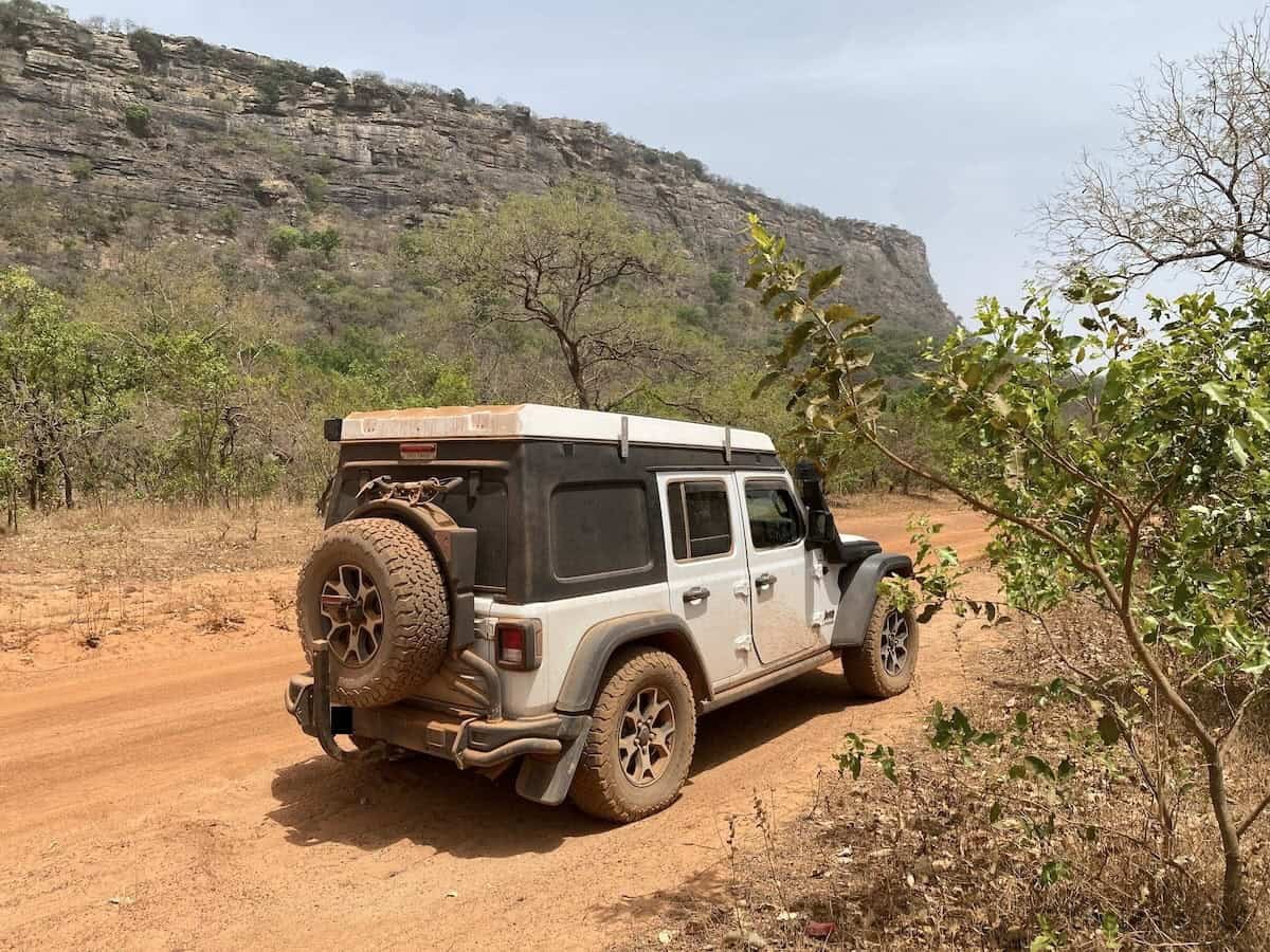 Overland Jeep driving on a red dirt road in Guinea with a rising road plateau ahead
