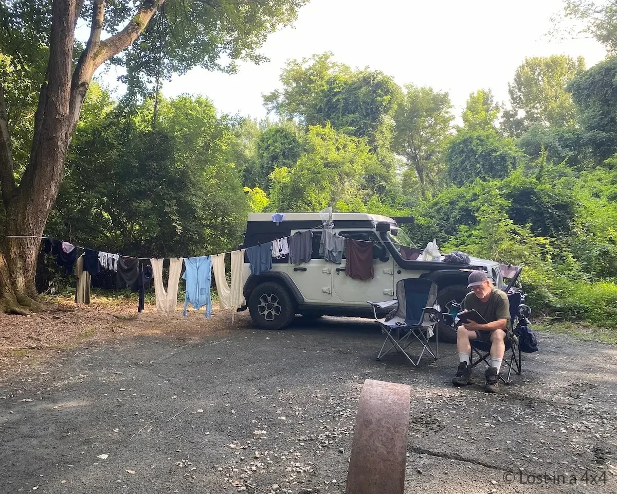 Wet clothes hanging on a laundry line between a Jeep and a tree at a campsite in the United States during a long-term overland journey.