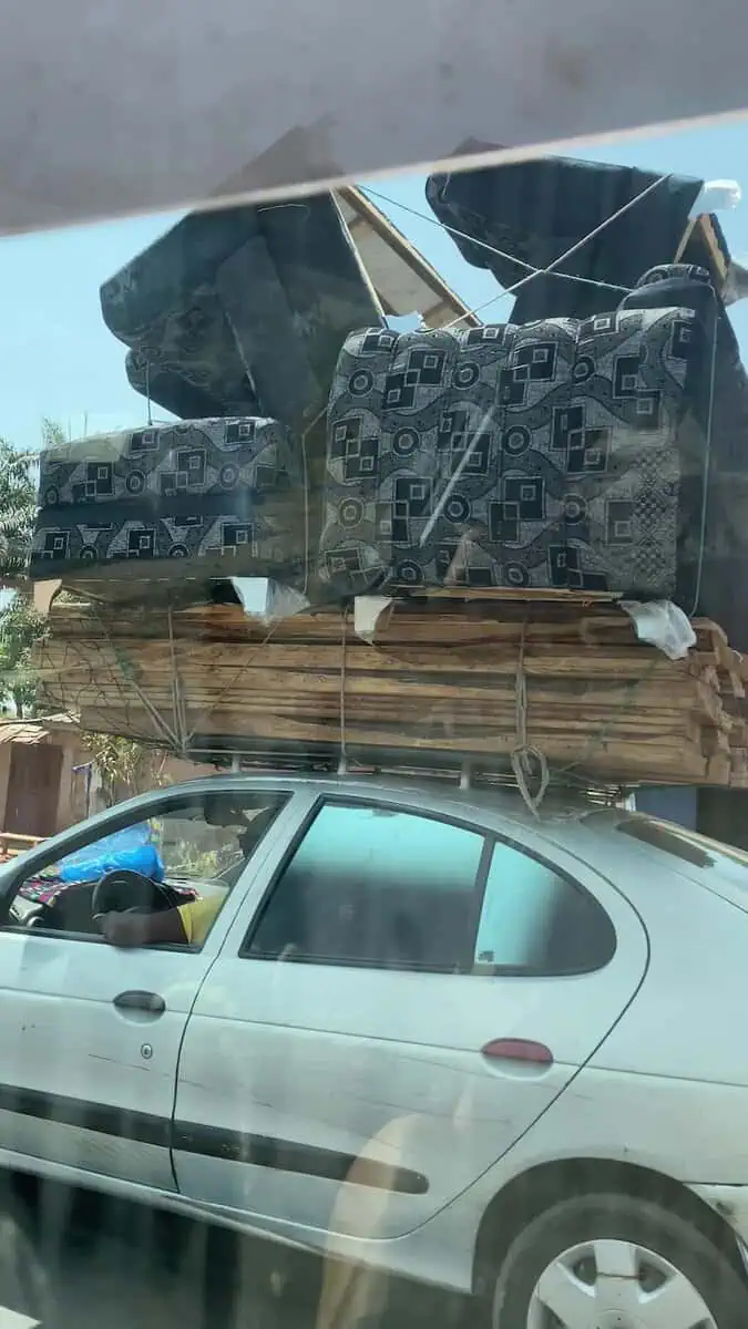 Side view of car carrying couches and wood panels on roof on road to Conakry Guinea
