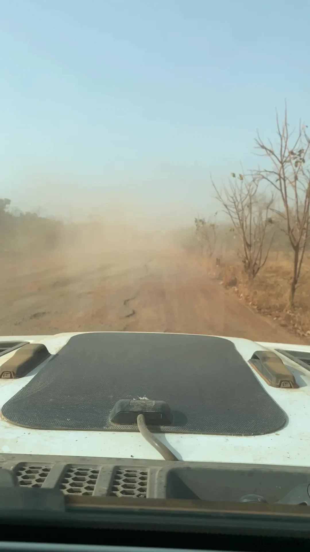 View from inside a Jeep showing a dusty, damaged tarmac road with potholes, highlighting challenging road conditions during overland travel.