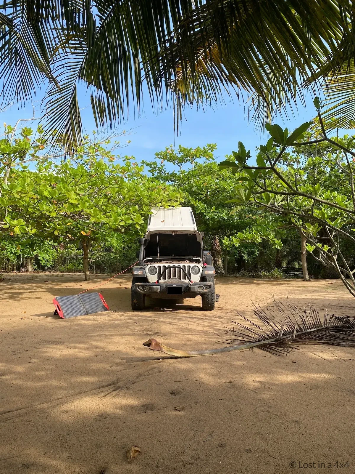 Portable Predator 100-watt solar panel connected to Jeep Genesis Offroad dual battery system charging at beach in Ivory Coast