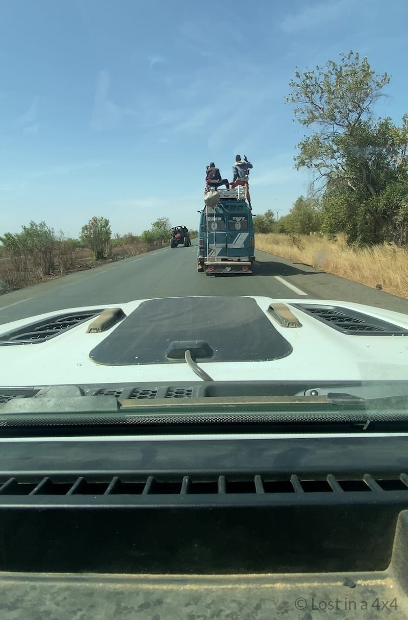 View from inside an overland Jeep of a local mini bus with passengers sitting on the roof driving on a road in Senegal