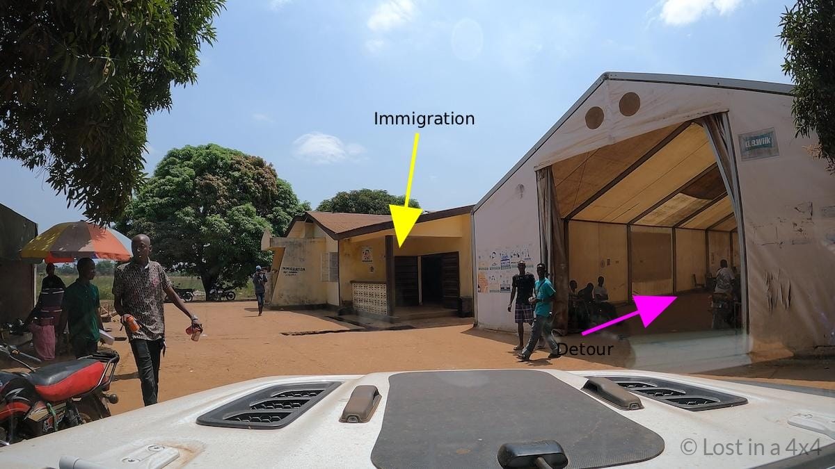 View from inside a Jeep showing the Sierra Leone immigration office ahead and a detour road during overland border crossing.