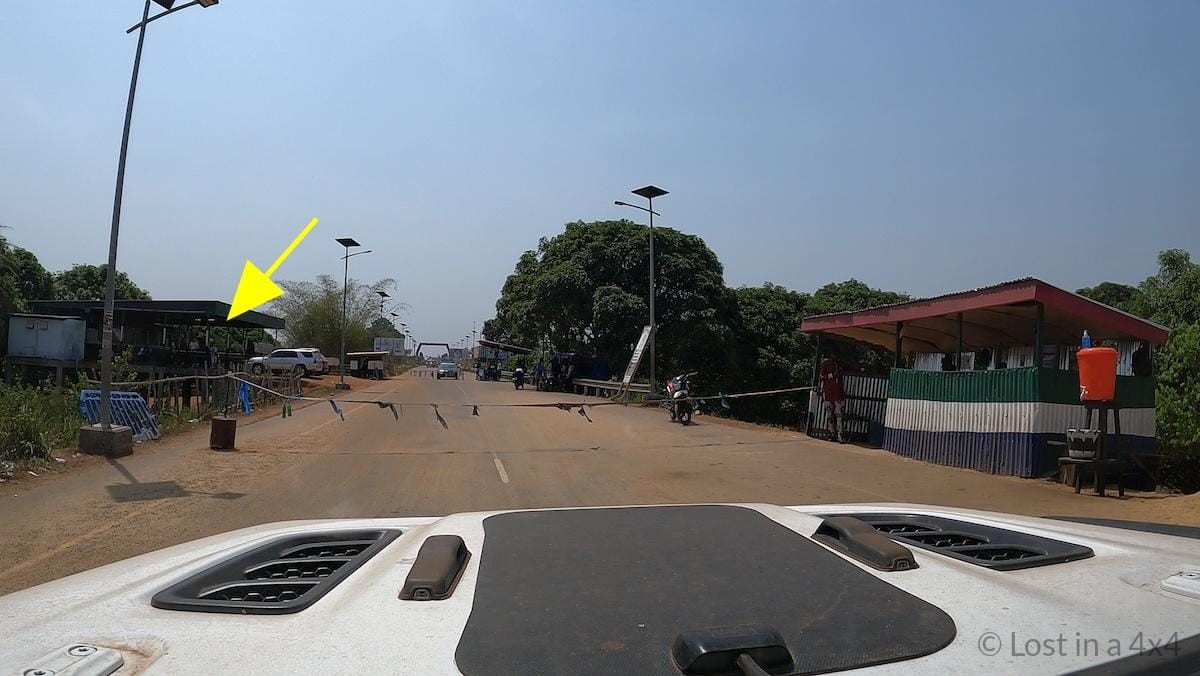 View from inside a Jeep approaching the Sierra Leone–Liberia border roadblock and customs office during overland travel.