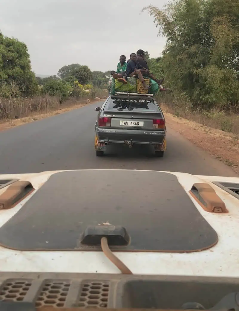 View from Jeep windshield of vehicle ahead with children sitting on roof on tarmac road to Conakry Guinea