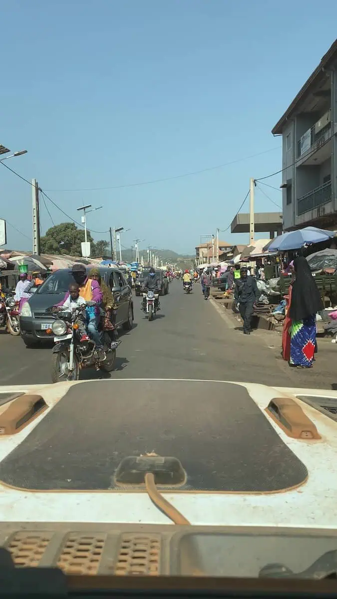 View from Jeep windshield of car and motorcycles including child passenger invading lane on tarmac road to Conakry Guinea