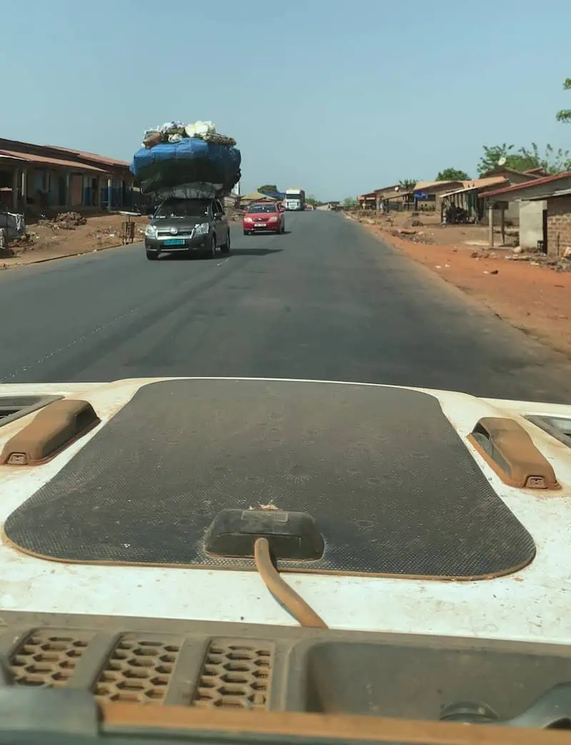 View from Jeep windshield of car with oversized roof load on tarmac road to Conakry Guinea