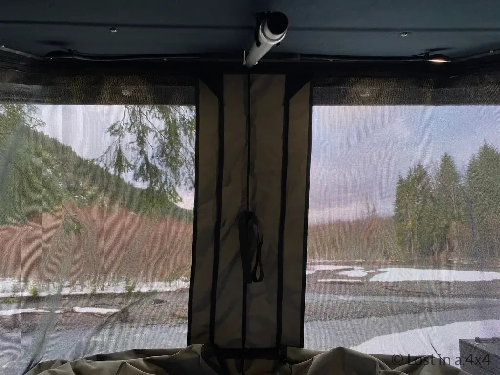 Interior view of Ursa Minor pop-top camper showing rear windows with mosquito nets in snowy camping conditions.