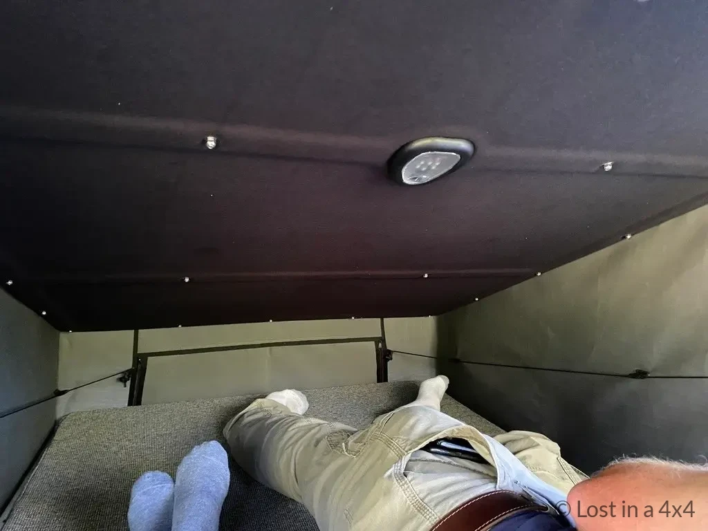 Interior view of Ursa Minor Jeep pop-top camper showing full bed length and front ventilation window.