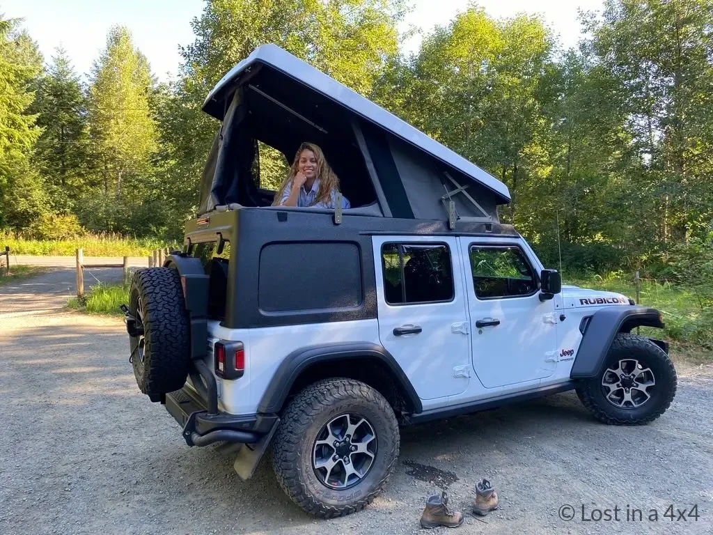 Karla relaxing inside an Ursa Minor pop-top camper with both rear windows open, showing access and exit options.