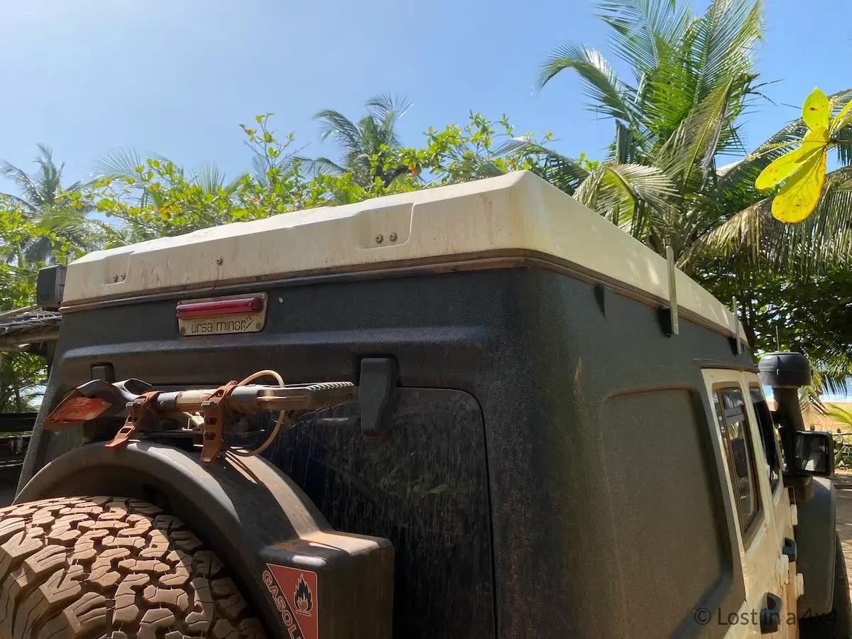 Close-up rear view of an Ursa Minor pop-top camper showing the roof tent design at a beach campsite in Ivory Coast.
