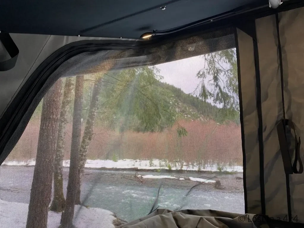 Interior view of the Ursa Minor pop-top camper side window with mosquito net during snowy camping conditions.