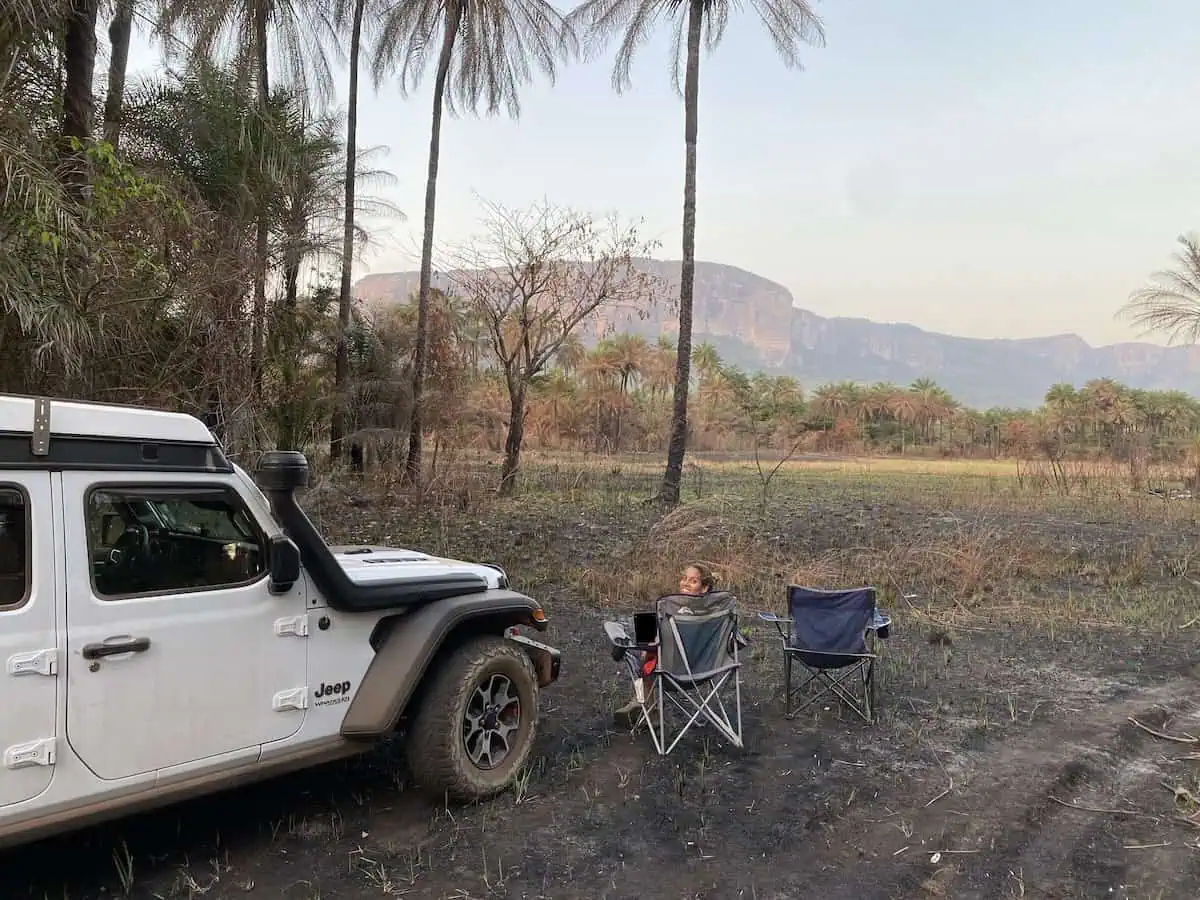 Karla sitting on camping chair beside Jeep Wrangler Rubicon with sheer cliff mountains in distance in Guinea